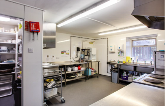 A kitchen with a fire extinguisher, shelving, and a window.